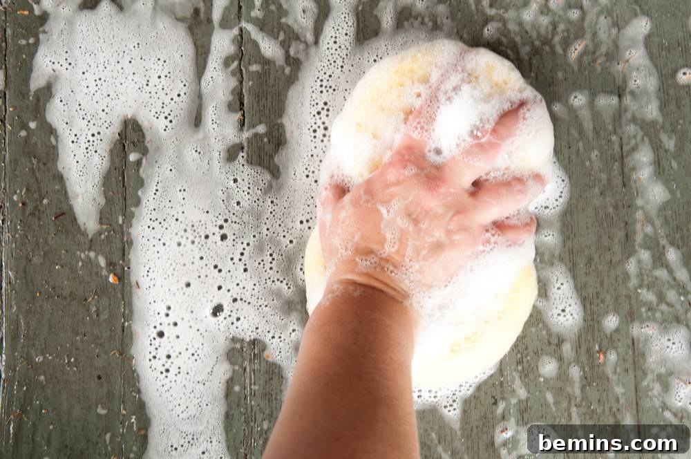 Hand holding a soapy sponge over a soapy wooden surface.