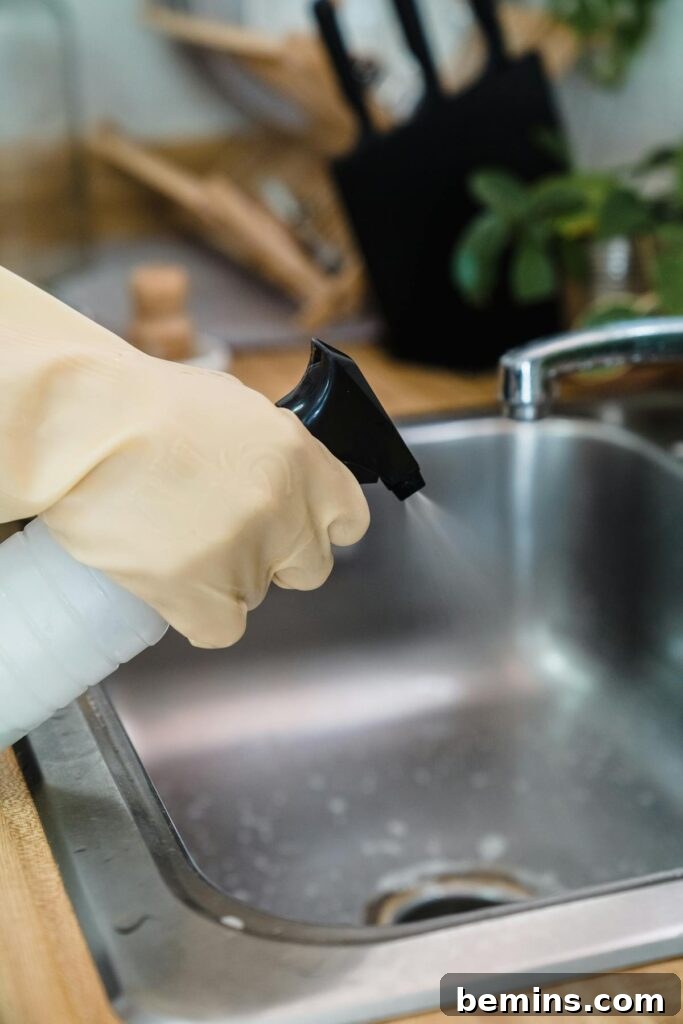 Close-up of a gloved hand cleaning a kitchen sink using a spray bottle, showcasing hygiene.